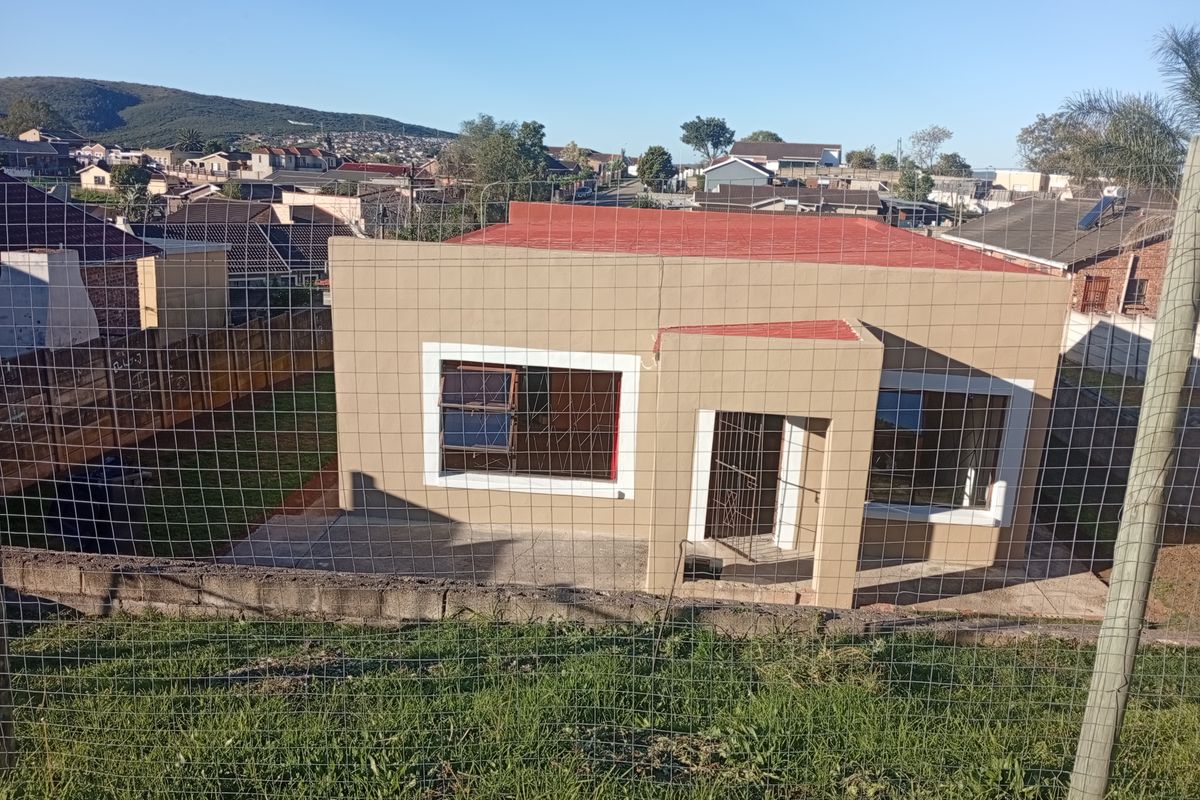 Rear view of a detached house featuring a concrete patio, aluminium window frames, and a metal roof, set within a fenced residential plot.