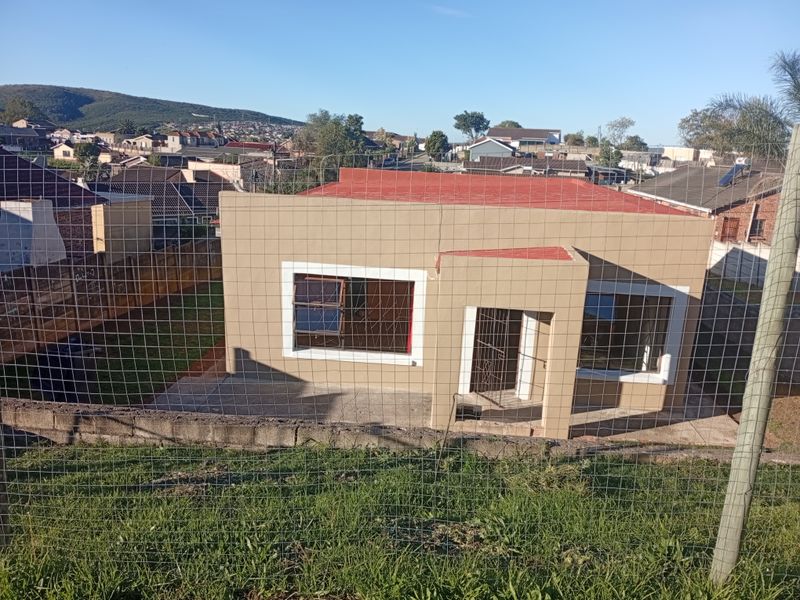 Rear view of a detached house featuring a concrete patio, aluminium window frames, and a metal roof, set within a fenced residential plot.