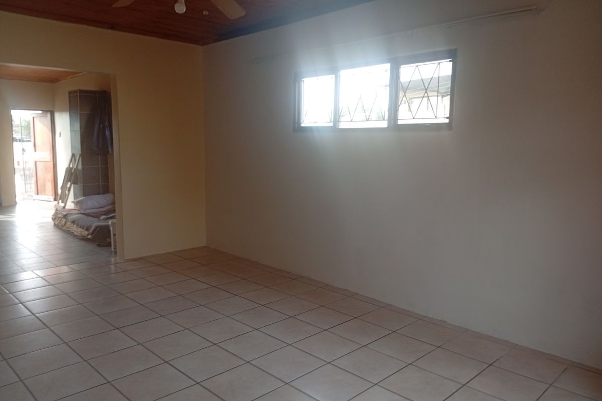 An empty living room featuring tiled flooring, a timber ceiling with a fan, and windows fitted with security bars.