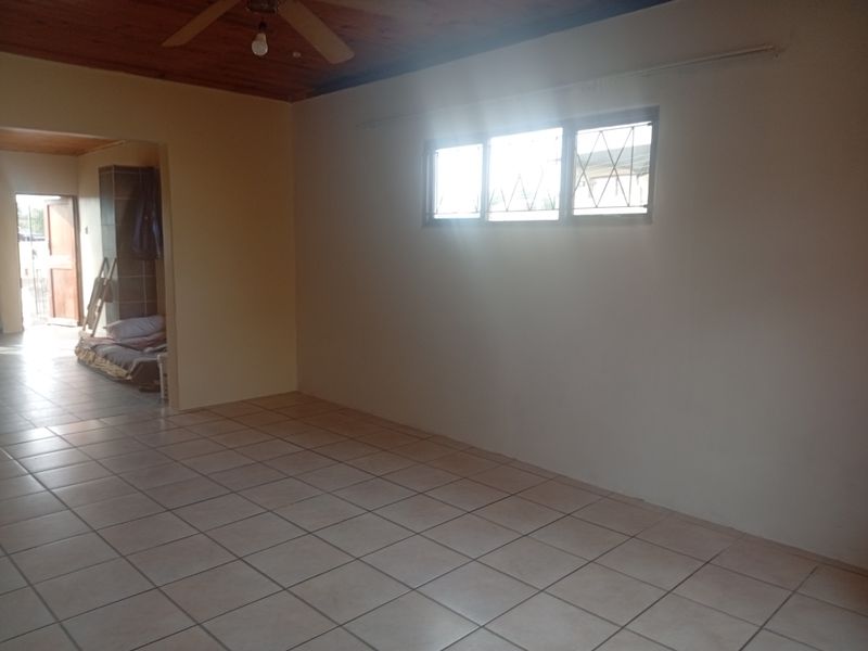 An empty living room featuring tiled flooring, a timber ceiling with a fan, and windows fitted with security bars.