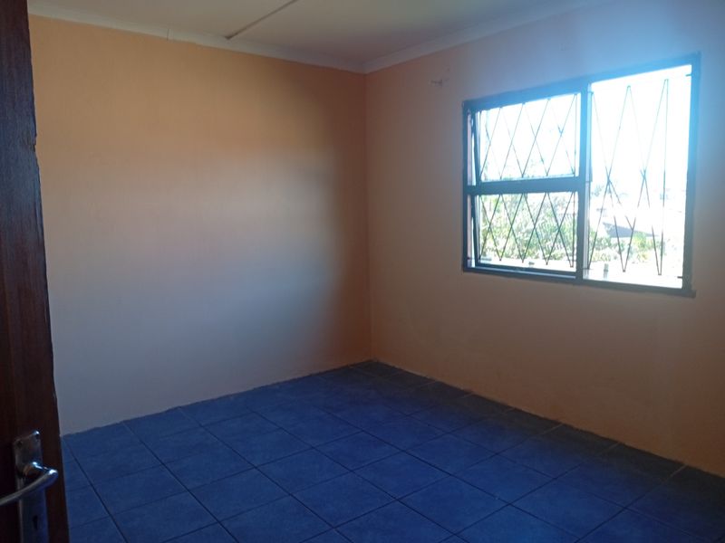 An empty bedroom featuring tiled flooring and a window fitted with security bars.