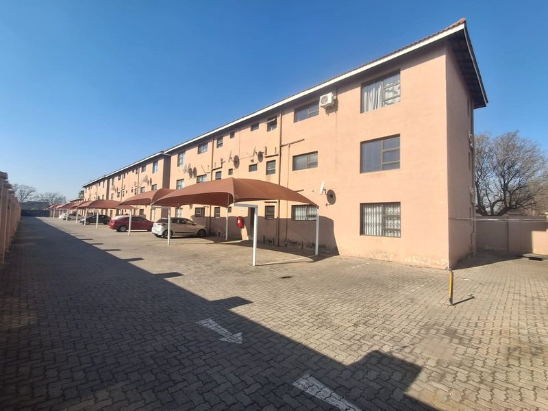 Exterior view of a multi-story residential flat complex featuring paved parking areas with shade sail carports and security-fitted windows.
