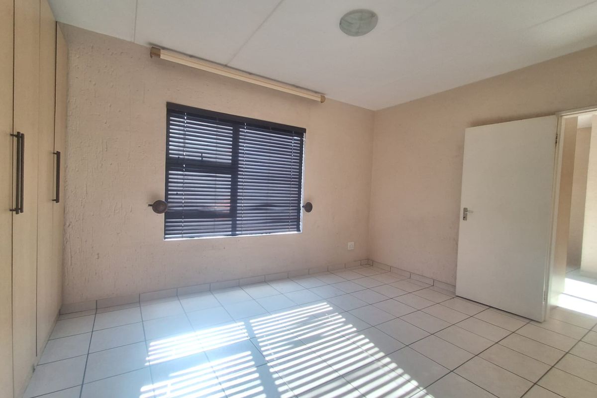 A bright, empty bedroom featuring tiled flooring, built-in cupboards, and venetian blinds on the window.