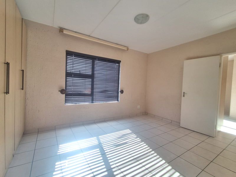 A bright, empty bedroom featuring tiled flooring, built-in cupboards, and venetian blinds on the window.