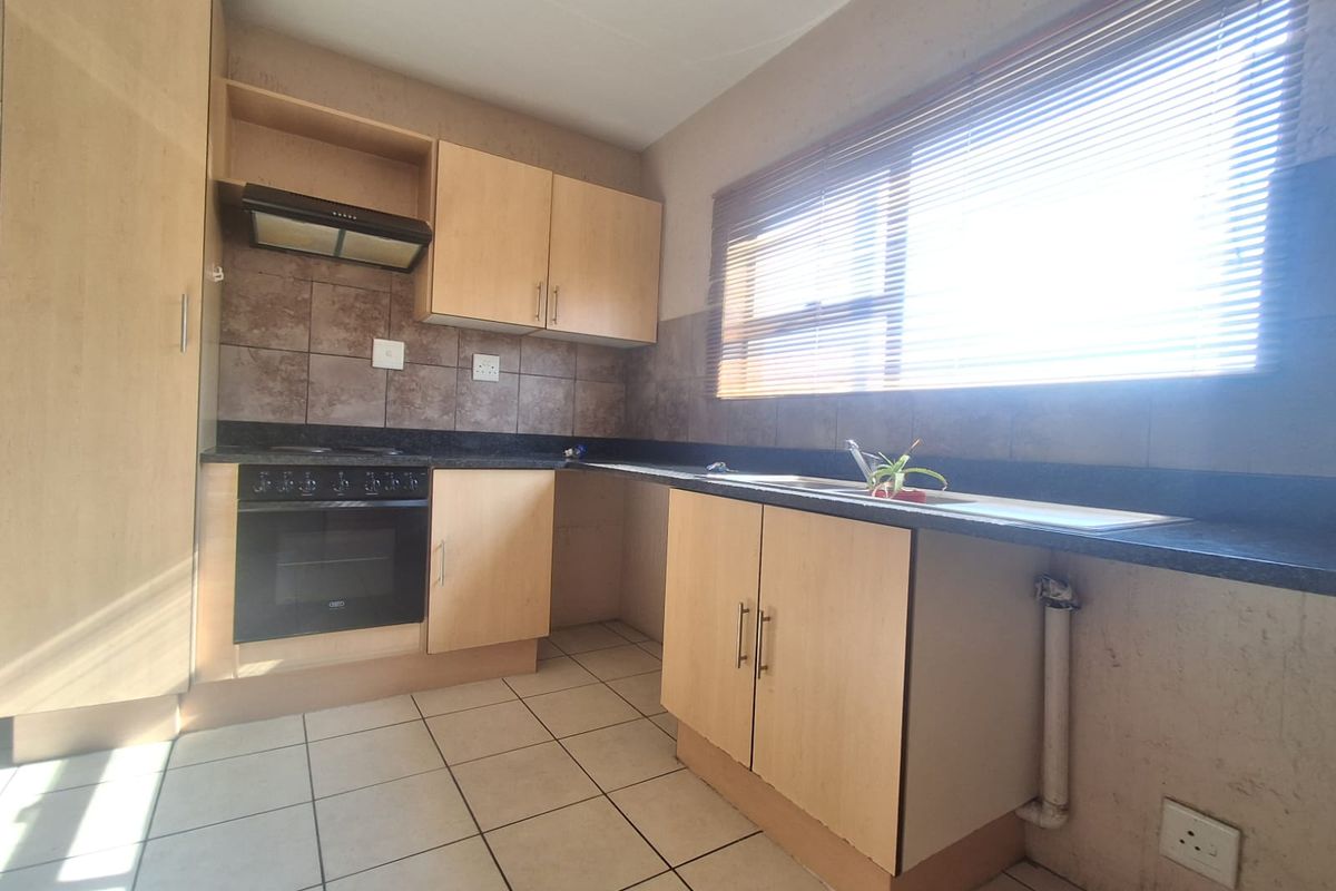 A functional kitchen featuring light wood-tone cabinetry, dark laminate countertops, a built-in oven with extractor fan, and tiled flooring.