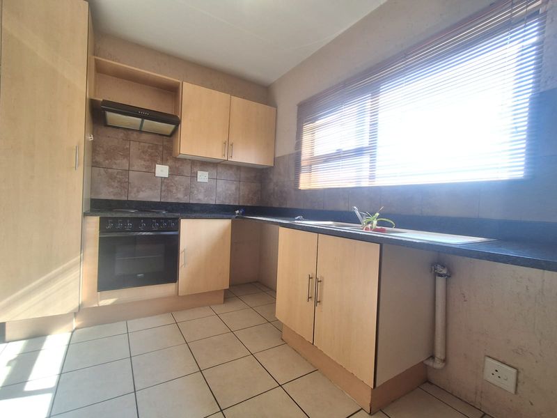 A functional kitchen featuring light wood-tone cabinetry, dark laminate countertops, a built-in oven with extractor fan, and tiled flooring.