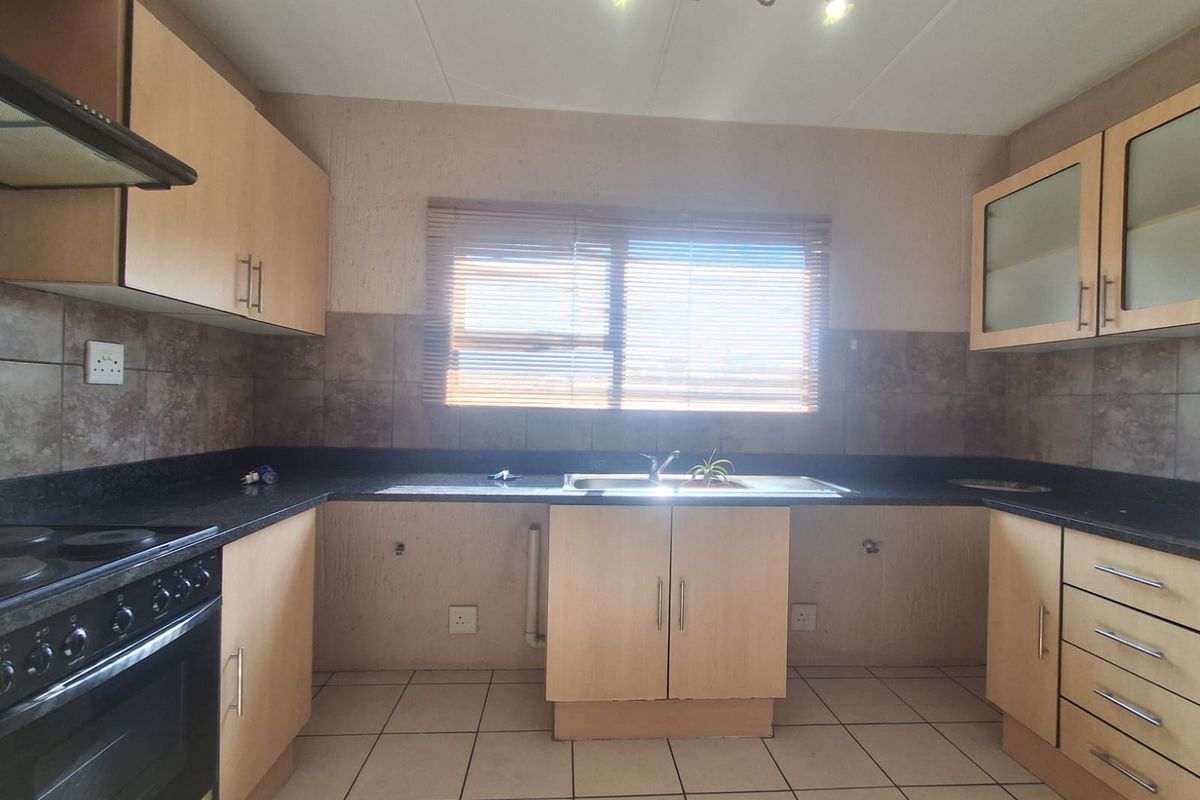 A functional kitchen featuring built-in cabinetry, dark countertops, a double sink, and integrated oven and hob, with tiled flooring and splashbacks.