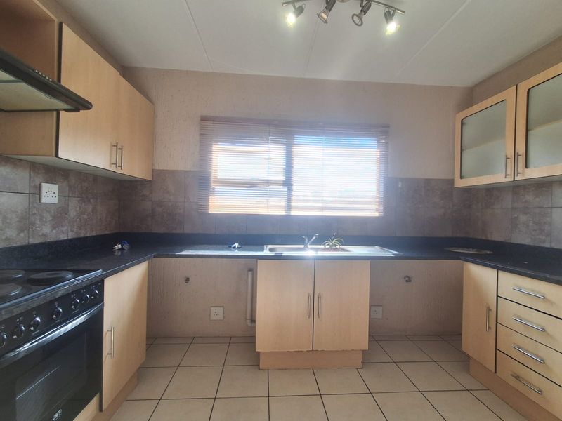 A functional kitchen featuring built-in cabinetry, dark countertops, a double sink, and integrated oven and hob, with tiled flooring and splashbacks.
