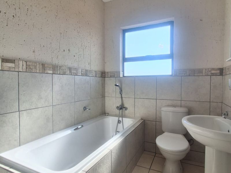 A functional bathroom featuring a bathtub, pedestal basin, and toilet with neutral wall and floor tiling.