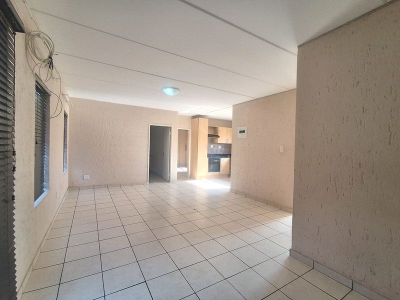 An open-plan living and kitchen area featuring tiled flooring, textured walls, and built-in kitchen cabinetry with an integrated oven and extractor fan.