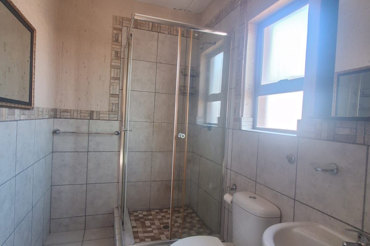 A functional bathroom featuring a shower enclosure, pedestal basin, and toilet with neutral tiled finishes, offering potential for modernization.