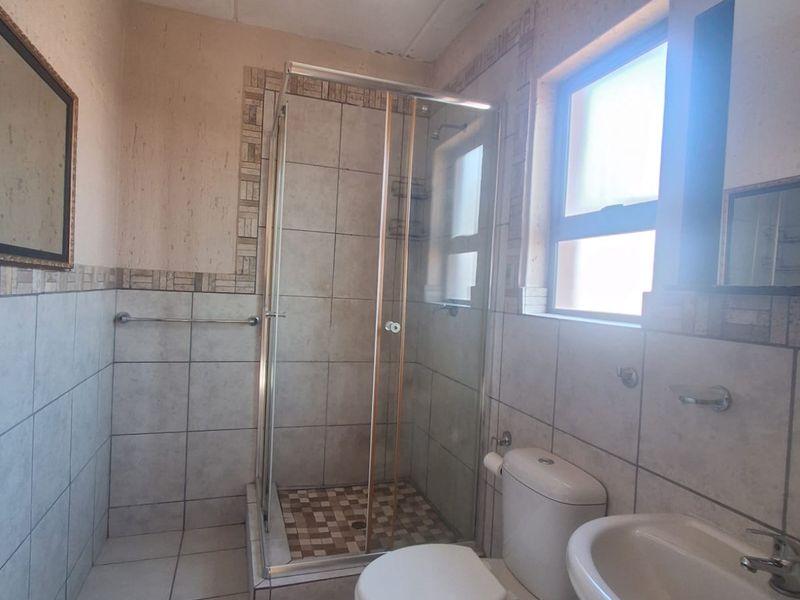 A functional bathroom featuring a shower enclosure, pedestal basin, and toilet with neutral tiled finishes, offering potential for modernization.