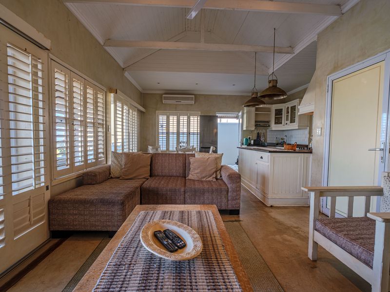 Open-plan living and kitchen area featuring vaulted timber ceilings, concrete floors, and plantation shutters, offering a relaxed coastal aesthetic.
