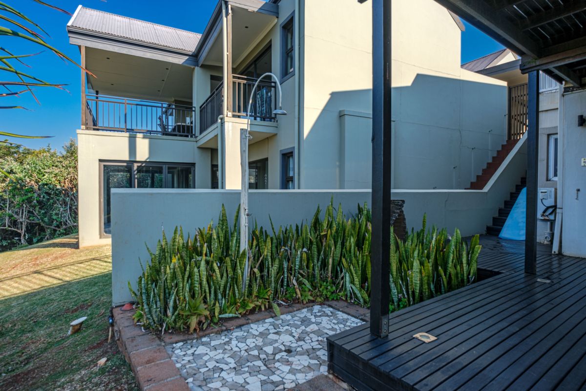 Rear exterior view featuring a timber deck, outdoor shower, stone paving, and a multi-level building structure with a balcony and staircase.