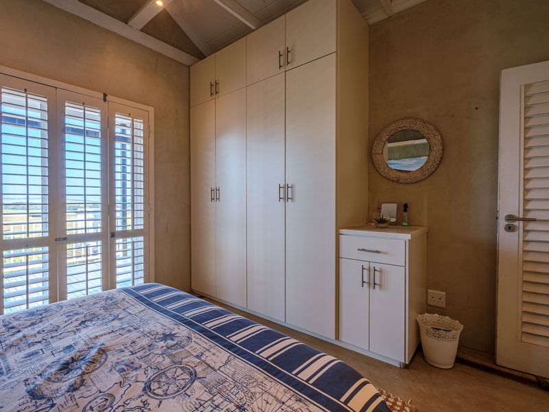 A bedroom featuring built-in cupboards, louvered shutters opening to a view, and an exposed beam ceiling with a neutral wall finish.