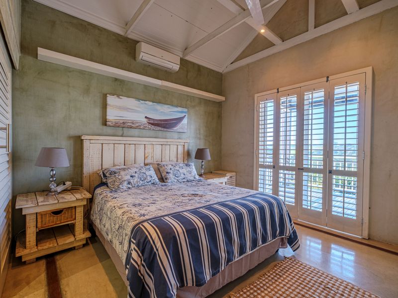 A well-maintained bedroom featuring vaulted ceilings with exposed rafters, polished concrete floors, and plantation shutters opening to an outdoor area.