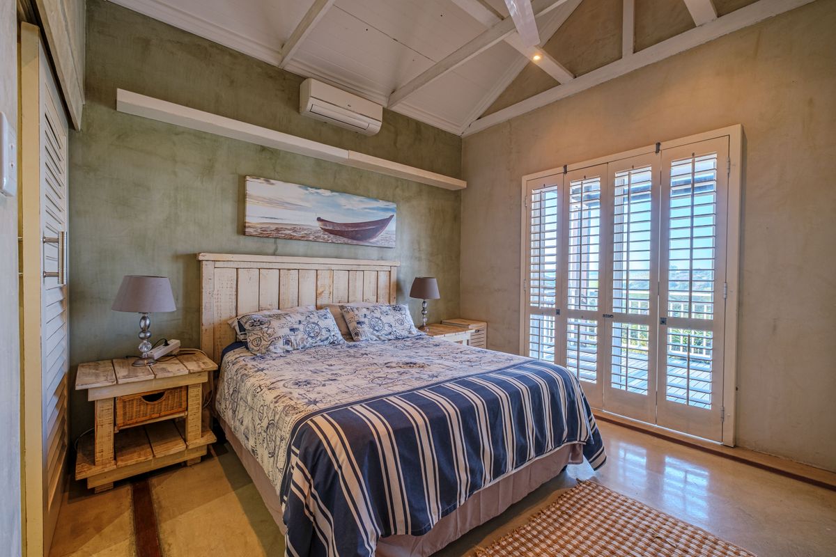 A well-maintained bedroom featuring vaulted ceilings with exposed rafters, polished concrete floors, and plantation shutters opening to an outdoor area.