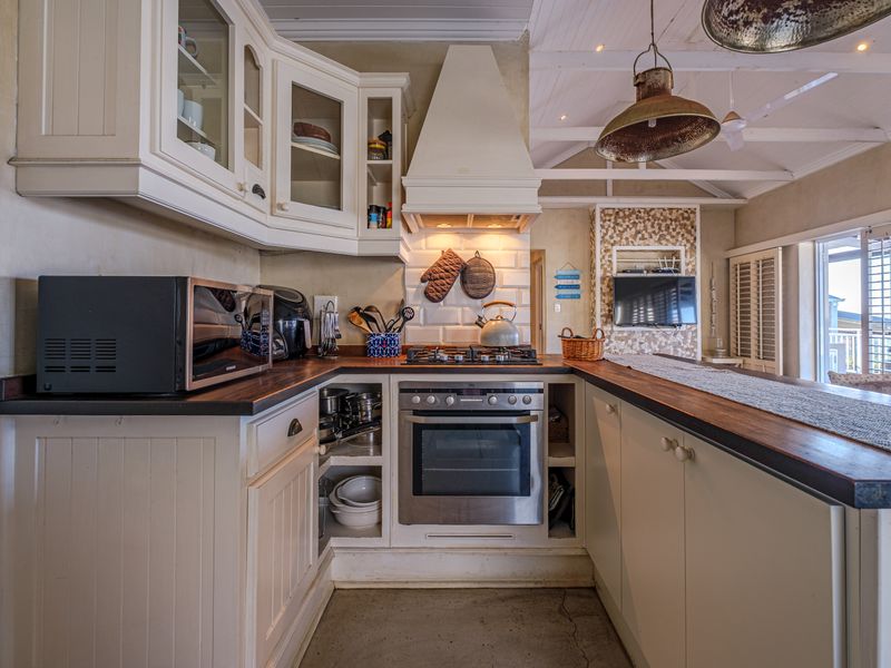 A charming kitchen featuring white cabinetry, timber countertops, a gas cooktop, and a subway tile backsplash under an exposed beam ceiling.