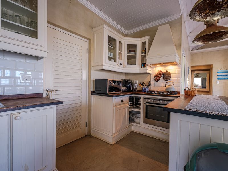 A rustic-style kitchen featuring white cabinetry, timber countertops, subway tile backsplash, and integrated cooking appliances under a tongue and groove ceiling.