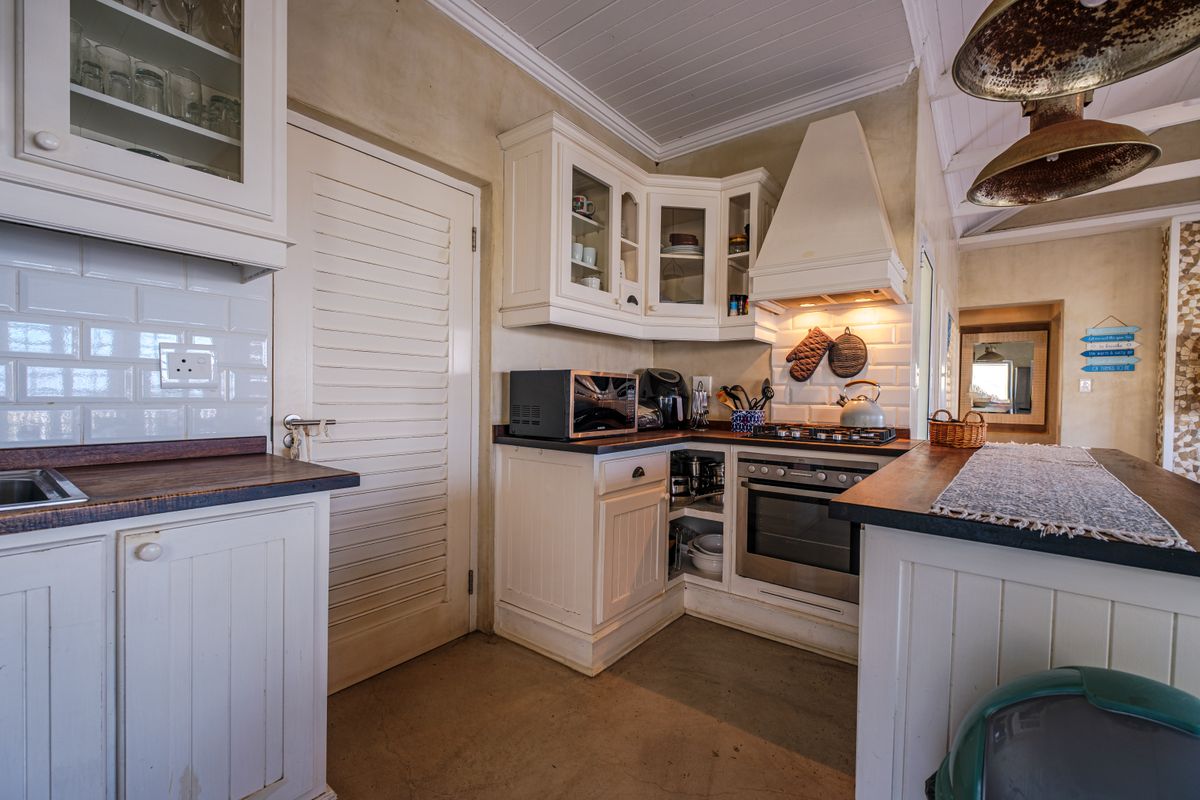 A rustic-style kitchen featuring white cabinetry, timber countertops, subway tile backsplash, and integrated cooking appliances under a tongue and groove ceiling.