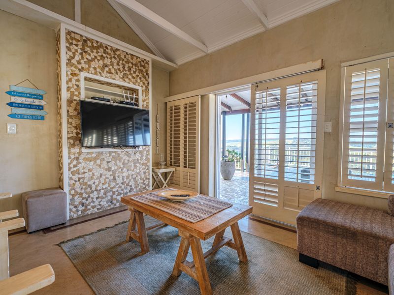 A cozy living room featuring a unique stone accent wall, vaulted ceilings with exposed rafters, and sliding plantation shutters opening to an outdoor patio.