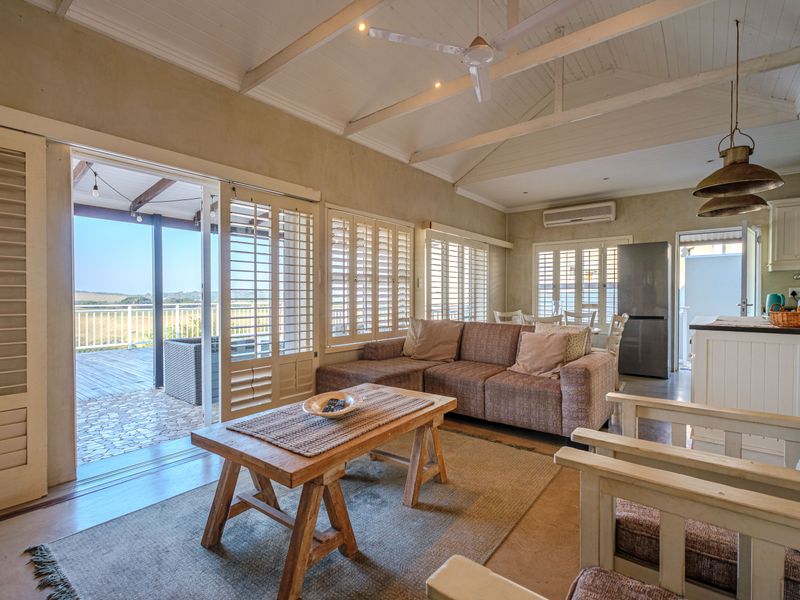Spacious open-plan living area featuring vaulted ceilings with exposed beams, plantation shutters, and seamless flow to an outdoor patio.