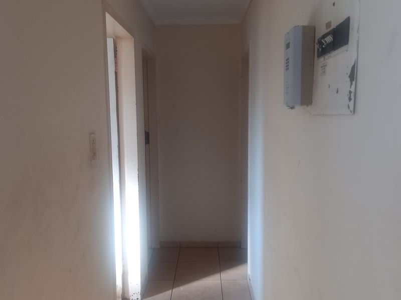 A narrow interior hallway featuring tiled flooring, a ceiling access hatch, and a wall-mounted electrical distribution board.