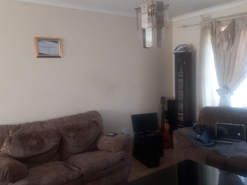 A living room area featuring tiled flooring and a central chandelier, requiring cosmetic updates to the walls and ceiling to improve the overall aesthetic.