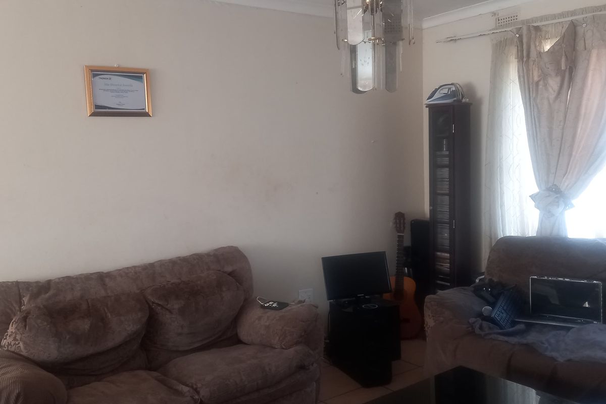 A living room area featuring tiled flooring and a central chandelier, requiring cosmetic updates to the walls and ceiling to improve the overall aesthetic.