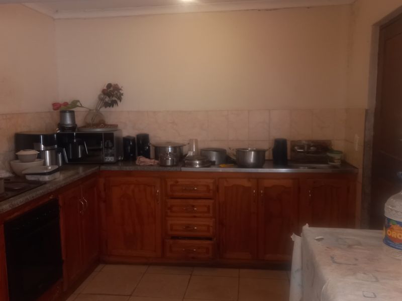 A functional kitchen featuring wooden cabinetry, tiled splashbacks, and ceramic flooring, offering a dated aesthetic with potential for modernization.