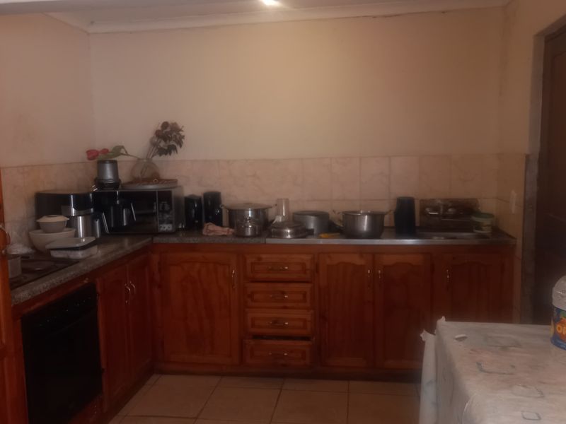 A dated kitchen featuring wooden cabinetry, tiled backsplash, and tiled flooring, offering a functional layout with built-in oven and sink area.