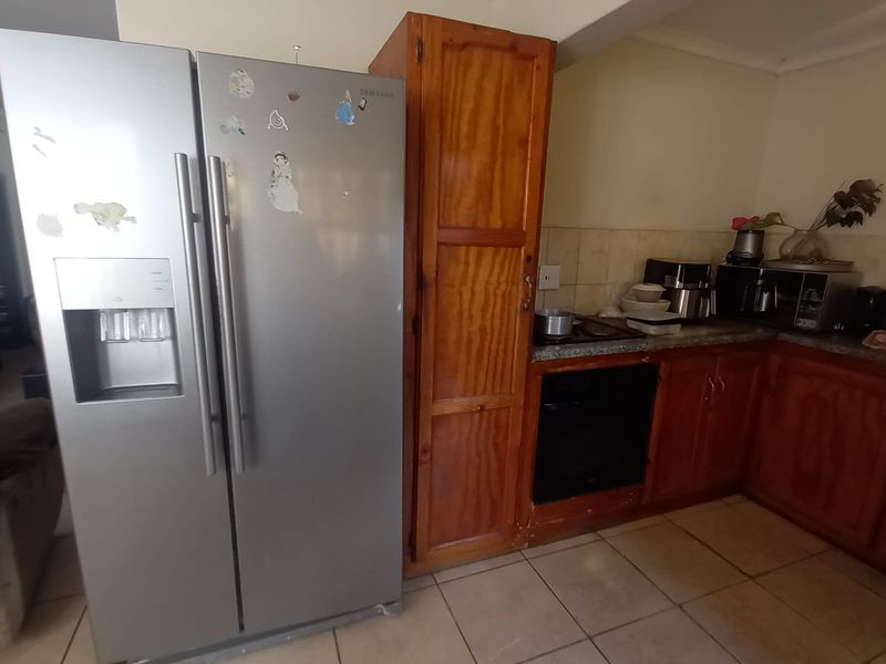 A functional kitchen featuring wooden cabinetry, tiled flooring, and built-in oven and hob, offering a traditional layout with potential for modern updates.