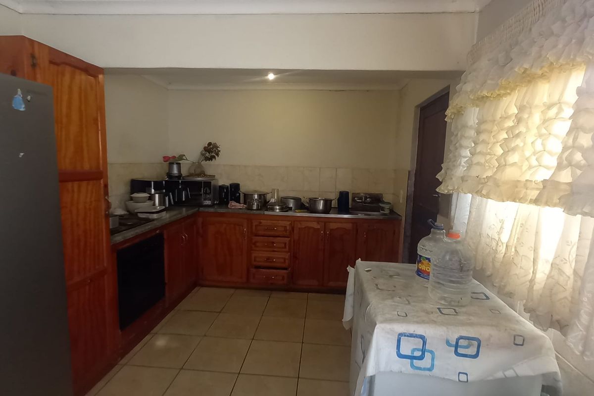 A functional kitchen featuring wooden cabinetry, tiled flooring, and a tiled backsplash, offering a dated aesthetic with potential for modernization.