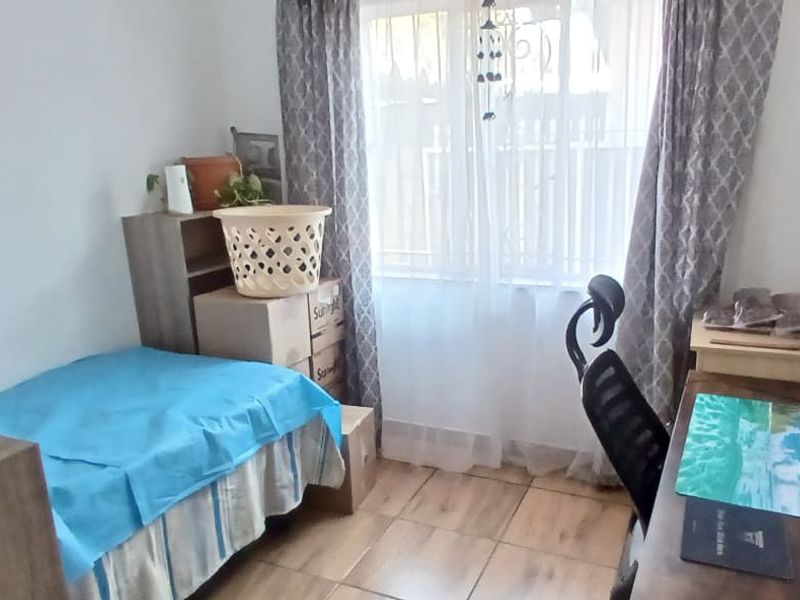 A functional bedroom featuring tiled flooring and natural light through a window with curtain rails.