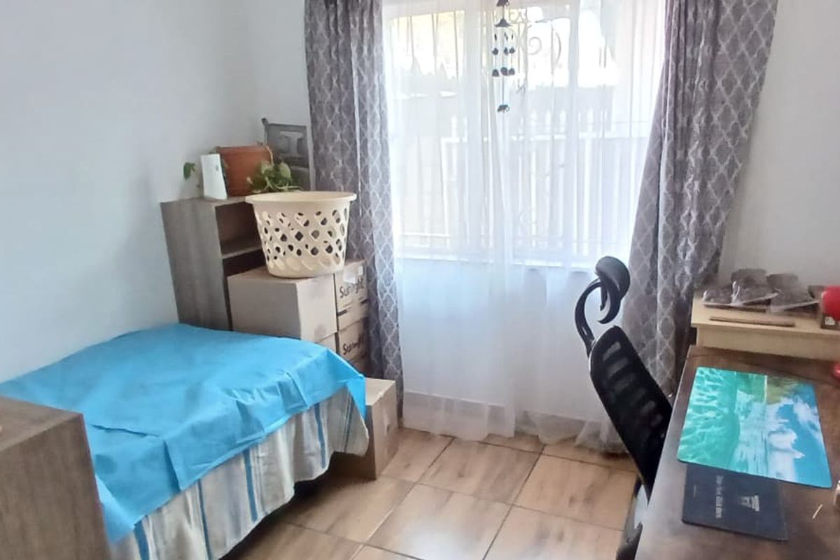 A functional bedroom featuring tiled flooring and natural light through a window with curtain rails.