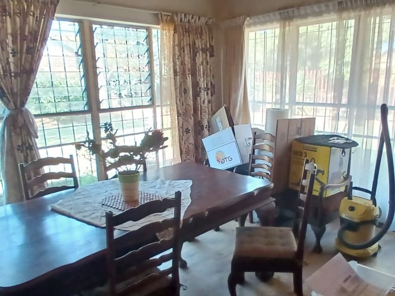 A dining room featuring large windows with security bars, providing ample natural light and views of the garden.