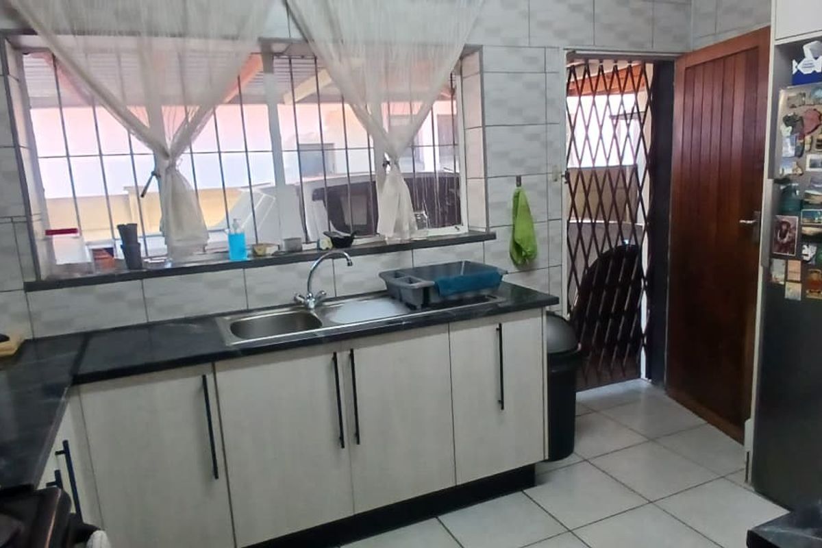 A functional kitchen featuring built-in cabinetry, tiled backsplash, and tiled flooring, with direct access to an exterior area through a security gate.