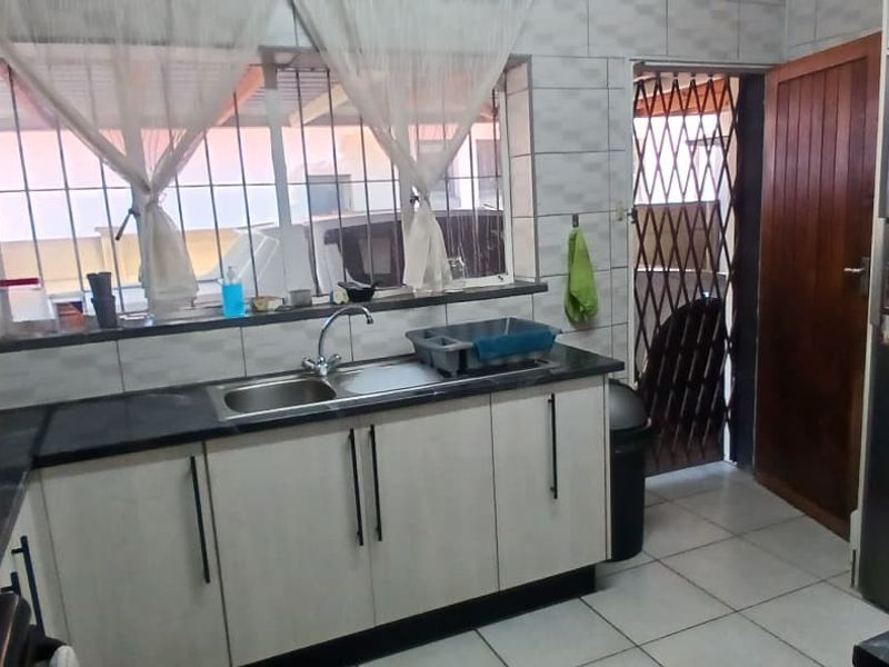 A functional kitchen featuring built-in cabinetry, tiled backsplash, and tiled flooring, with direct access to an exterior area through a security gate.