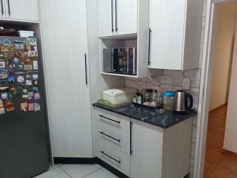 A functional kitchen area featuring modern white cabinetry, dark laminate countertops, a built-in microwave, and tiled finishes throughout.