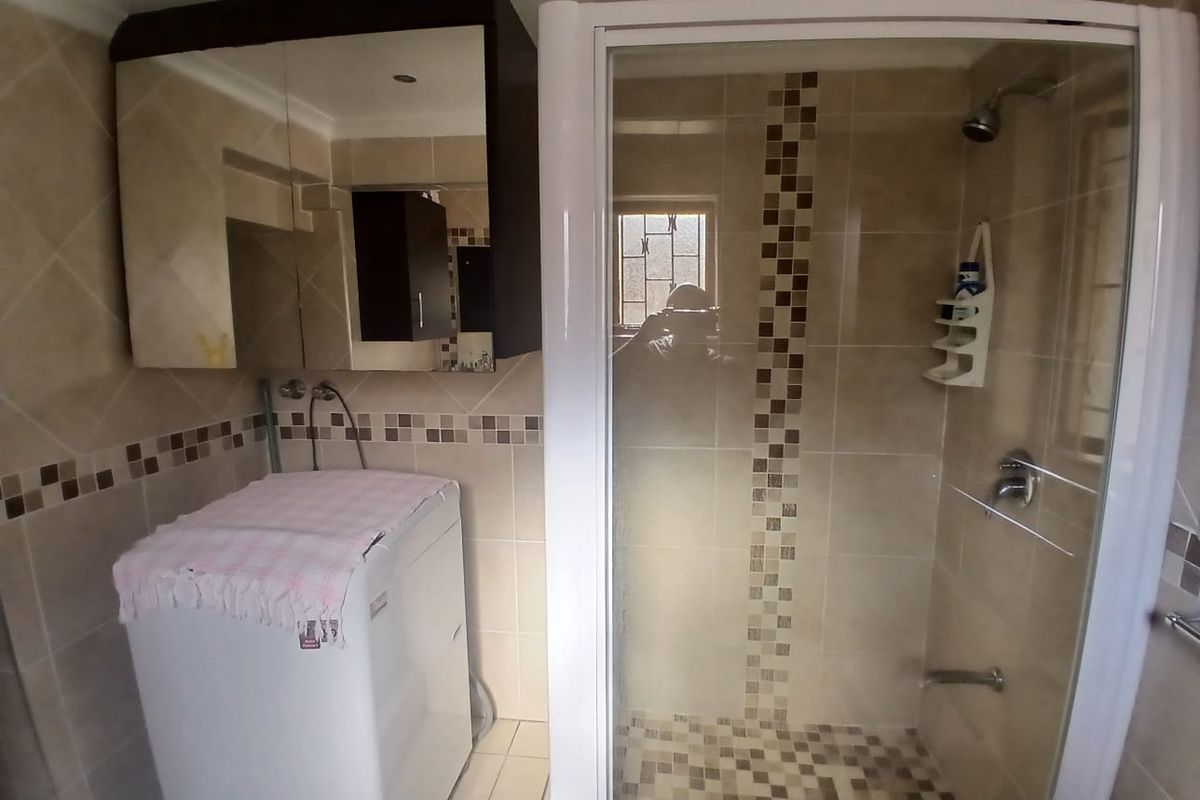 A functional bathroom featuring a glass-enclosed shower, tiled finishes, and a wall-mounted vanity cabinet with integrated mirror storage.