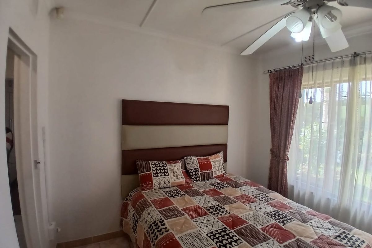 A functional bedroom featuring tiled flooring, a ceiling fan, and large windows with curtain rails, offering a comfortable and well-lit living space.