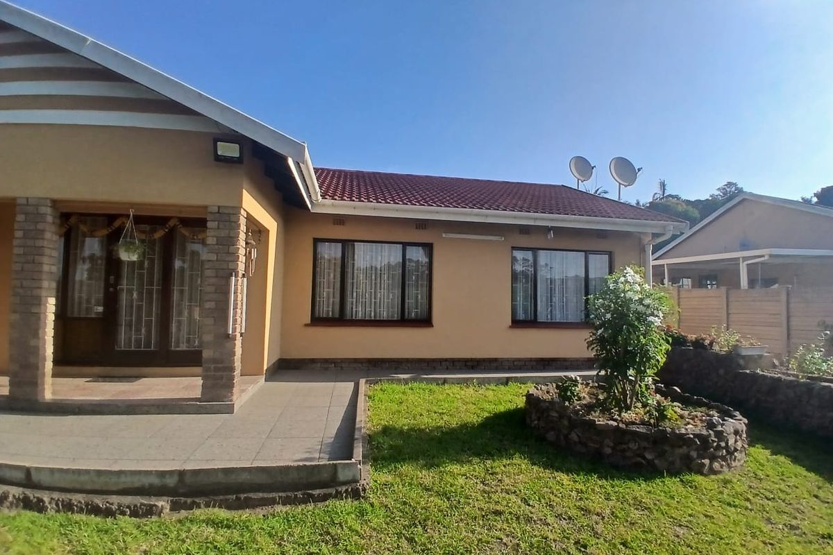 Rear view of the house featuring a covered patio, a landscaped garden with a stone-walled flower bed, and a tiled roof.