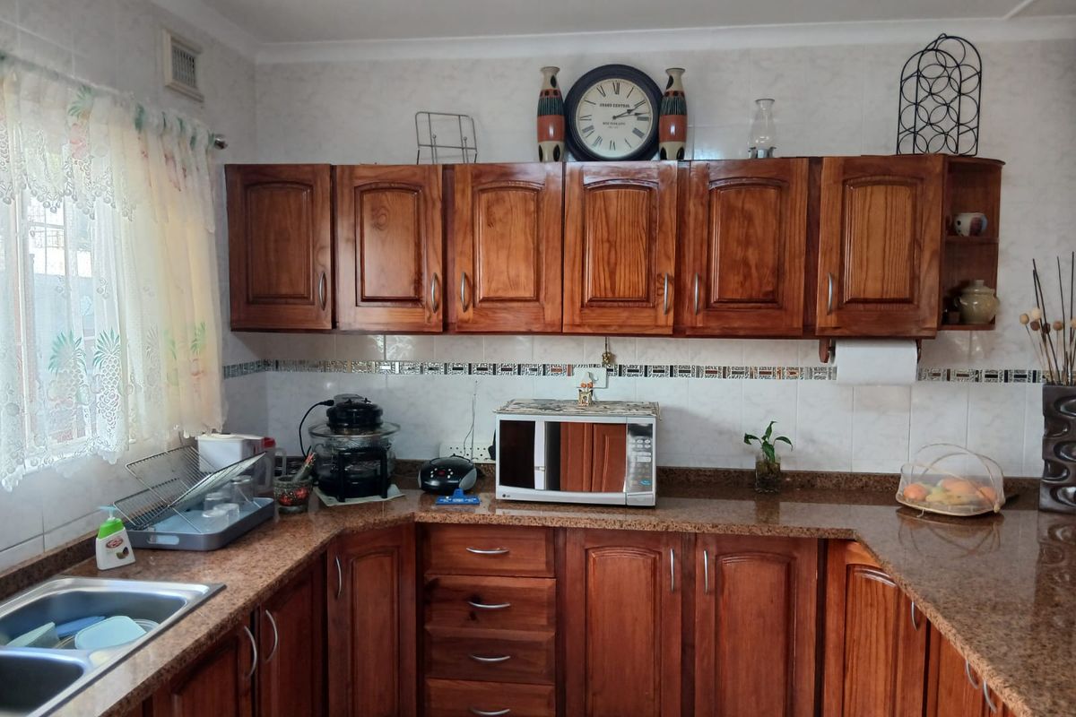 A functional kitchen featuring warm-toned wooden cabinetry, granite countertops, and a double bowl stainless steel sink with a decorative tiled backsplash.