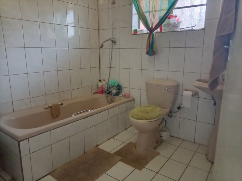 A functional bathroom featuring a bathtub, toilet, and pedestal basin with classic white wall tiling and floor tiles.