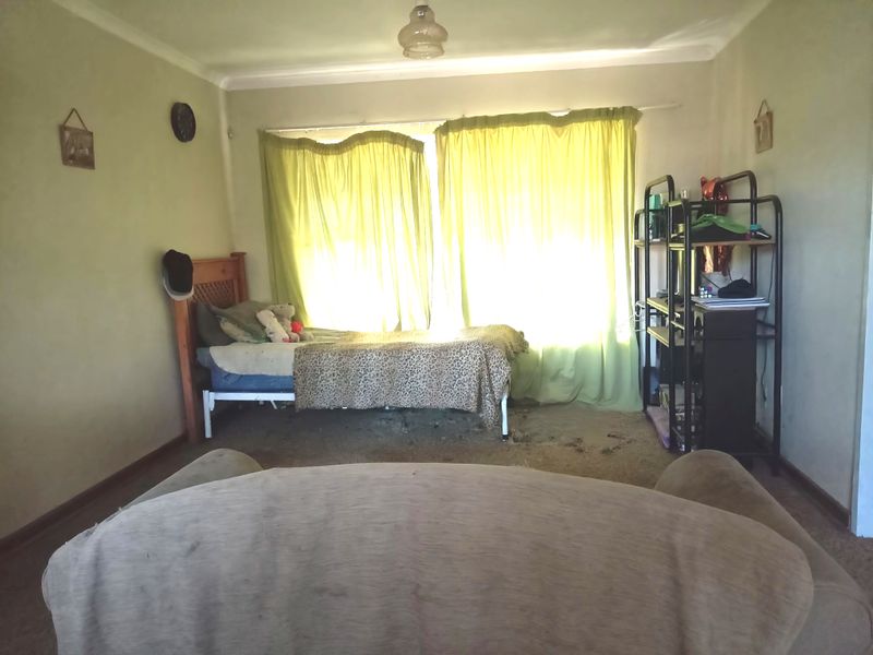 A bedroom featuring carpeted flooring and large windows with curtains, requiring cosmetic updates to improve the overall condition and appeal.