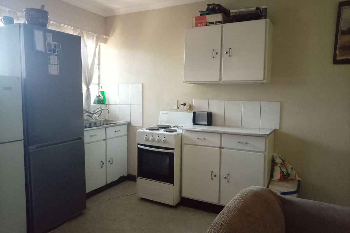 A functional kitchen featuring white cabinetry, a tiled splashback, and a freestanding stove, offering potential for modernization and aesthetic improvement.