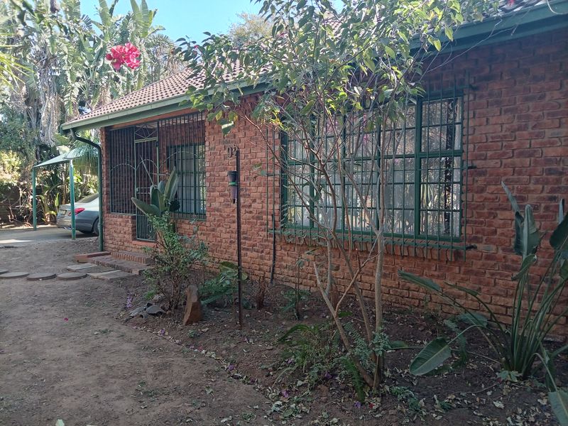 Front elevation of a face brick house featuring a tiled roof and security bars on windows and doors, set within a garden area.