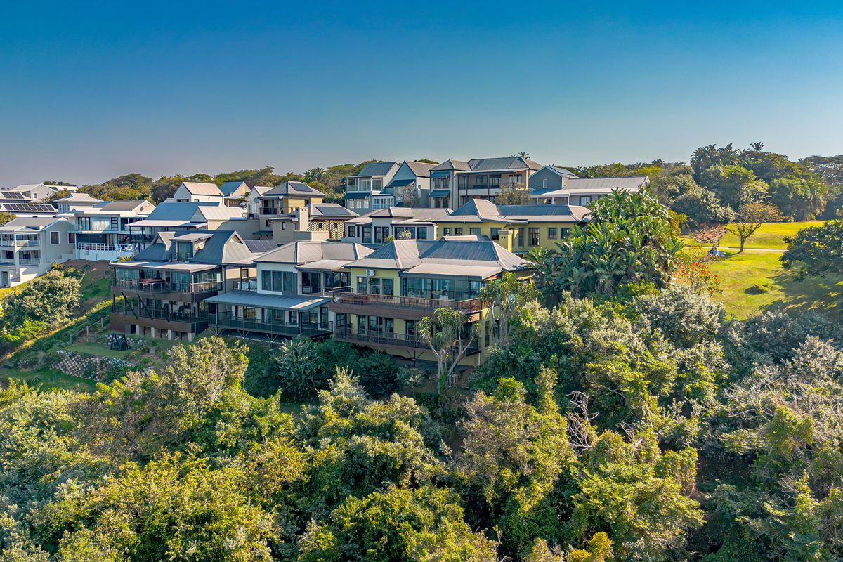 Aerial view of a residential estate featuring multi-level homes with metal roofing, expansive balconies, and lush surrounding greenery.