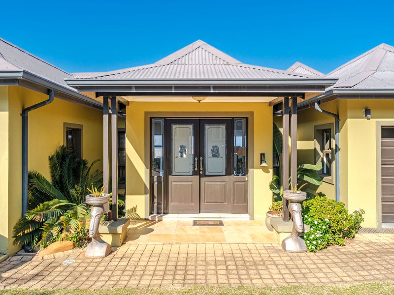 The front entrance features a covered porch with tiled flooring, double doors with glass inserts, and a well-maintained yellow facade under a metal roof.