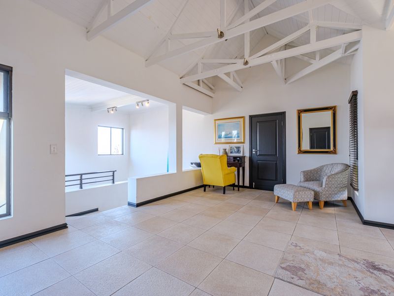 Spacious living area featuring high vaulted ceilings with exposed white timber trusses, neutral tiled flooring, and large windows providing ample natural light.